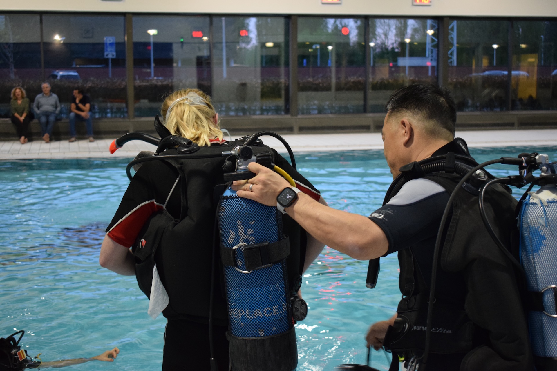 Duikinstructeur helpt student met uitrusting aan de rand van het zwembad