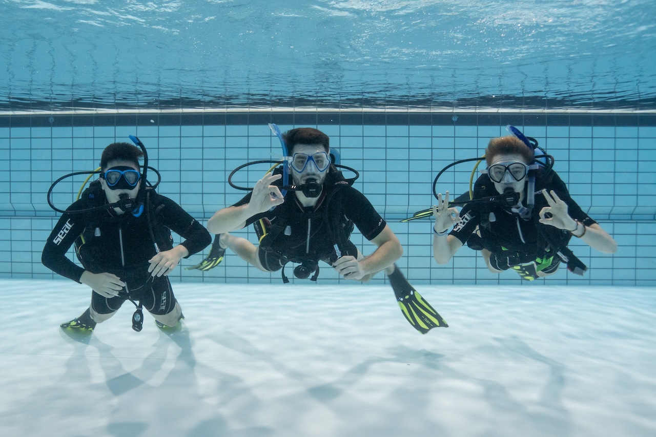 Drie duikstudenten zweven uitgetrimd onder water in het zwembad